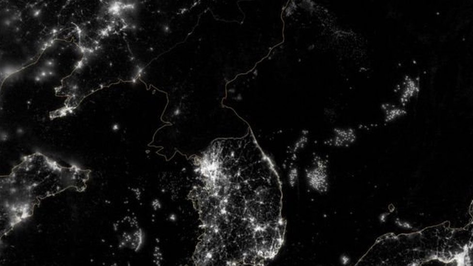 ஒளி மின்னும் ஷென்யாங் நகரத்திற்கும், சோலுக்கு இடையில் கருங்குழி இருப்பது போன்று வட கொரியா தோன்றும் படம்