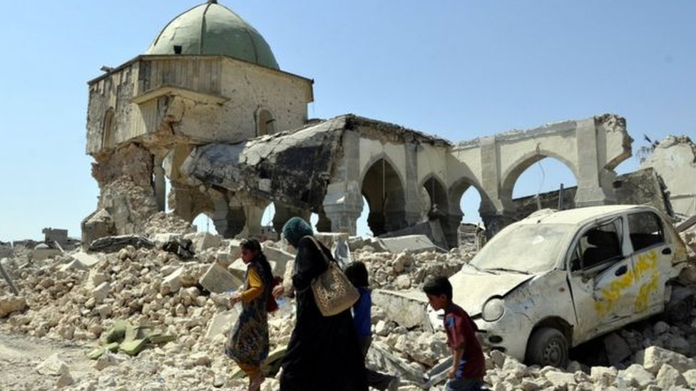 இடிபாடுகளின் ஊடாக செல்லும் மக்கள்